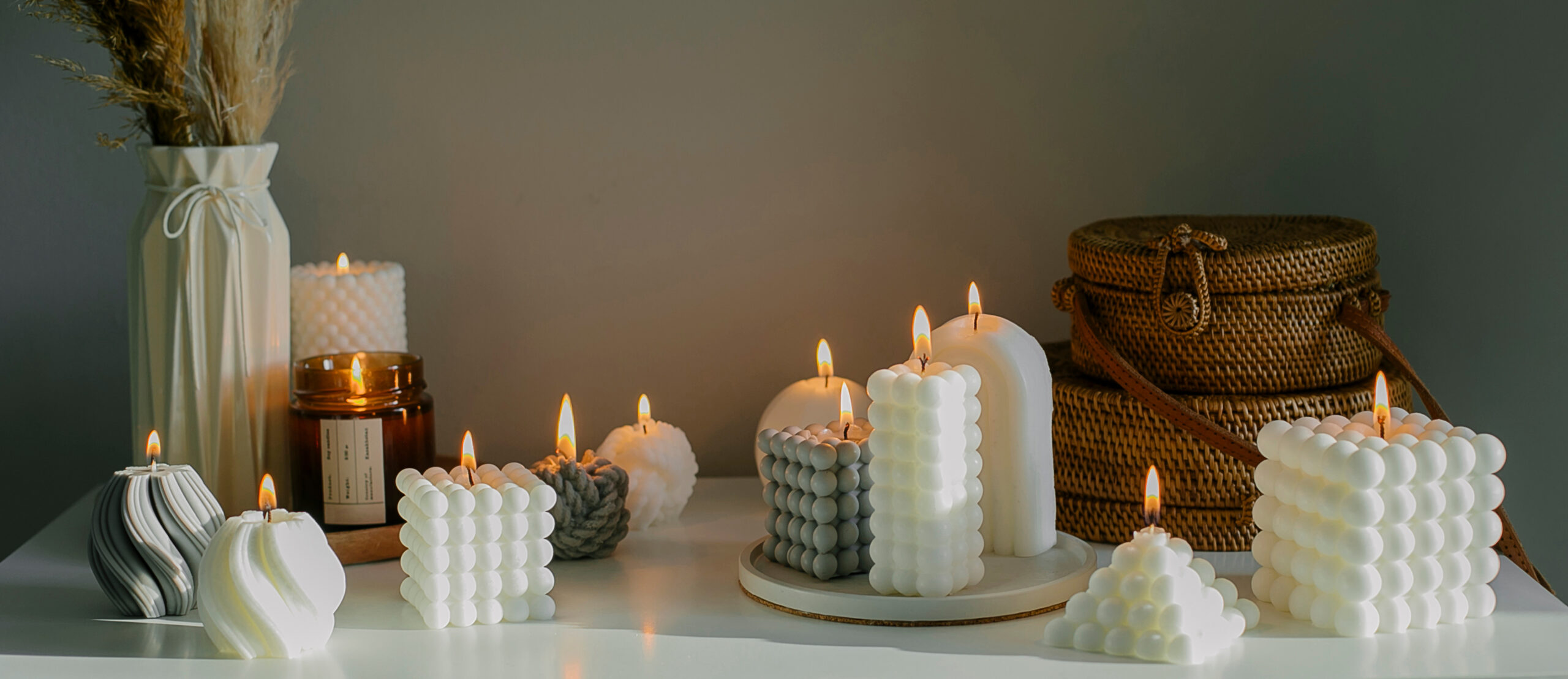 Banner image. Home interior decor. White dresser with dried flowers in vase, rattan bags and variety candles. Still life, hygge concept