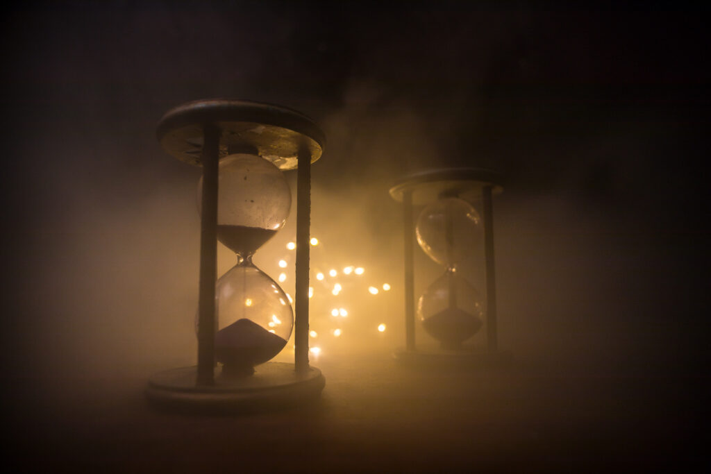 Time concept. Silhouette of Hourglass clock and old vintage wood clock with arrow and smoke on dark background with hot yellow orange red blue cold back lighting, or symbols of time with copy space
